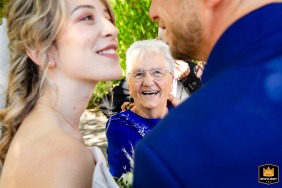 At the exit of the town hall in Tarn-et-Garonne, a grandmother smiles warmly as she watches her granddaughter share a kiss with her soon-to-be husband, capturing a touching intergenerational connection on the wedding day.